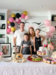 a family standing in front of a table with cakes and cupcakes on it