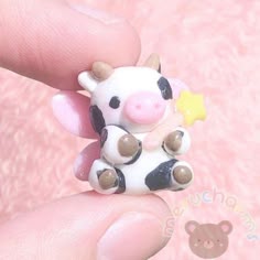 a tiny toy cow sitting on top of someone's finger in front of a pink background