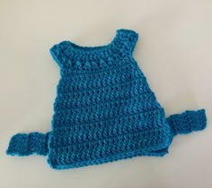 a blue crocheted baby dress sitting on top of a white table next to a pair of scissors