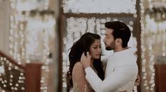 a man and woman standing next to each other in front of a wall covered with lights