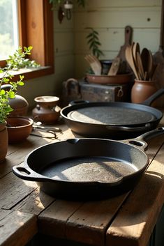 three cast iron skillets sitting on top of a wooden table next to potted plants