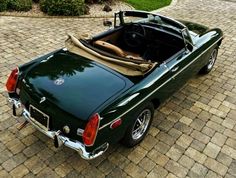 a green convertible car parked on top of a brick road
