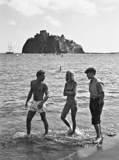 three people standing in the water near an island