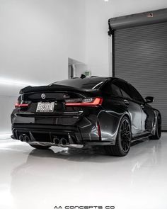 the rear end of a black sports car parked in a garage next to a roller door