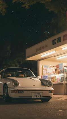 a white porsche parked in front of a store at night with the moon shining down