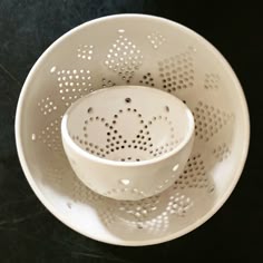a white bowl with holes in it on a black table