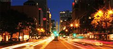 an empty city street at night time with lights streaking down the road and skyscrapers in the background