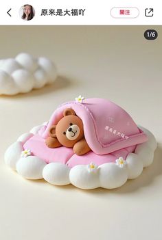 a teddy bear laying on top of a cloud shaped pillow with a pink blanket over it