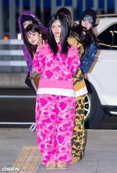 three young women dressed in pink and yellow outfits standing next to each other on the sidewalk