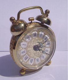 an old fashioned alarm clock with roman numerals on the face and hands, sitting on a white surface