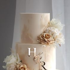 a three tiered wedding cake with flowers on the top and initials on the side