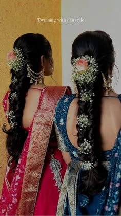 two women with braids and flowers in their hair, one wearing a blue sari