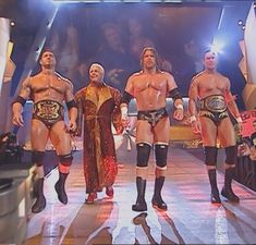 three men in wrestling gear standing next to each other on a stage with lights behind them