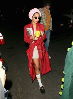 a woman in a red coat and white dress is holding a yellow box while walking