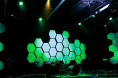 the stage is lit up with green lights and hexagonal shapes on it's sides