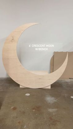 an unfinished wooden sculpture sitting on top of a floor next to a cardboard box with the words crescent moon written across it