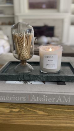 a candle sitting on top of a book next to a glass vase filled with matches