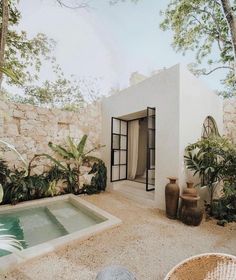 a small white house with a pool in the middle and plants around it on either side