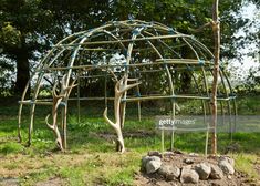 an outdoor structure made out of sticks and branches in the middle of a grassy area
