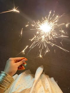 a person holding a sparkler in their hand while wearing a white dress and bracelets