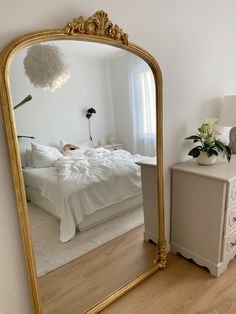a bedroom with a large gold mirror on the wall and a white bed in the background