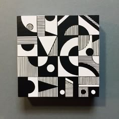 a square black and white painting on a gray wall with circles, lines, and shapes