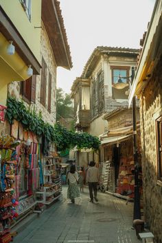 two people walking down an alley way with shops on both sides and buildings in the background