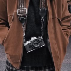 a person wearing a brown jacket and holding a camera in their hands with chains attached to them