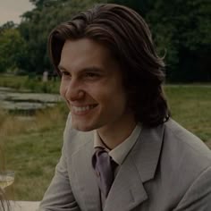 a man with long hair wearing a suit and tie sitting in front of a woman