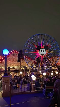the amusement park is lit up at night with mickey mouse on it's ferris wheel