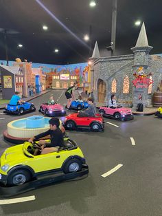 several people ride miniature cars on a toy town street at night with an amusement park in the background