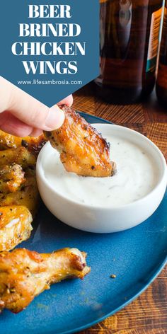 a person dipping chicken wings into a white sauce on a blue plate with beer bottles in the background