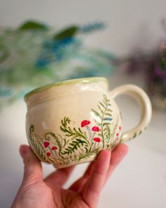 a hand holding a white cup with red flowers on the outside and green leaves on the inside