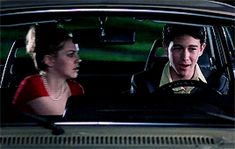 a young man and woman sitting in the back seat of a car looking at each other