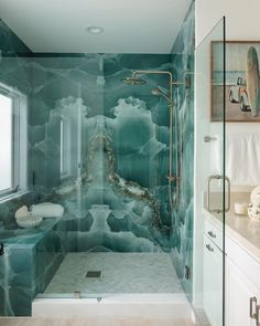 a bathroom with a glass shower door and blue marbled walls, along with white cabinets