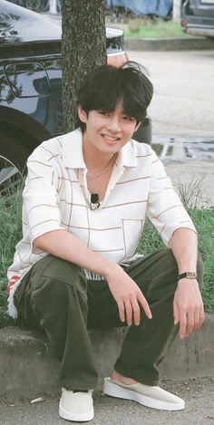 a young man sitting on the ground next to a tree