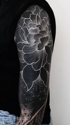 a man with a black and white flower tattoo on his arm is standing in front of a wall