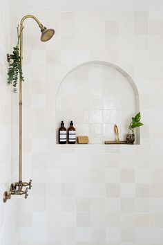a white tiled bathroom with gold faucet and shower head, soap dispenser on the wall