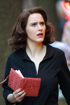 a woman in black shirt holding a red bag and looking off to the side with her hand on her hip