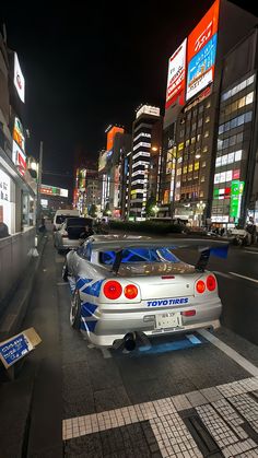 a silver car parked on the side of a road next to tall buildings at night