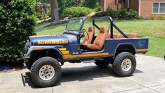 a blue jeep with brown leather seats parked in front of a brick house on a driveway
