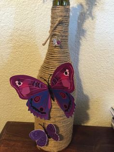 a wine bottle decorated with purple butterflies on a wooden table next to a white wall