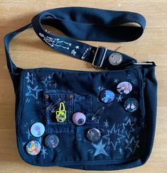 a black purse with buttons on it sitting on top of a wooden floor next to a lanyard