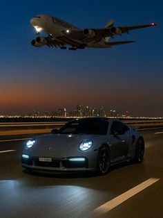 a large jetliner flying over a car on top of an airport runway at night