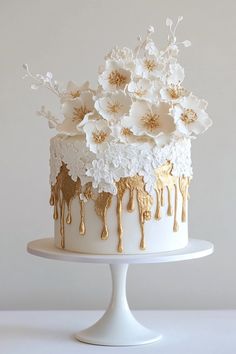a white cake with gold drips and flowers on the top is sitting on a plate