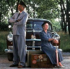 two people standing next to an old car