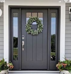 a gray front door with two planters and a wreath