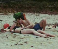 a man and woman laying on top of a sandy beach next to eachother