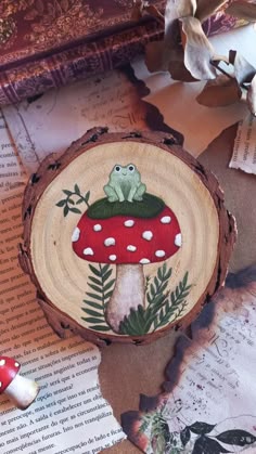 a wooden slice with a frog sitting on top of it next to mushrooms and leaves