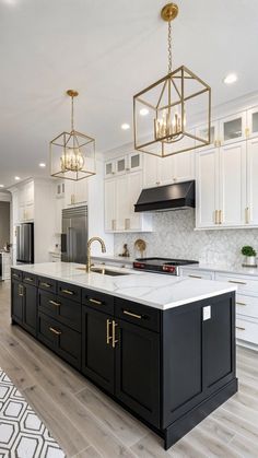 a large kitchen with white cabinets and black island in the center is lit by golden chandeliers